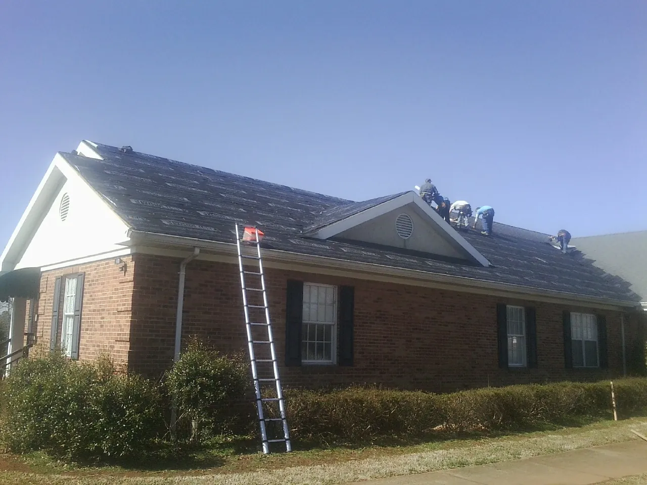 Crew tearing shingles off a brick ranch roof with a ladder set — Metal Roof Repair work by our crew in Delhi