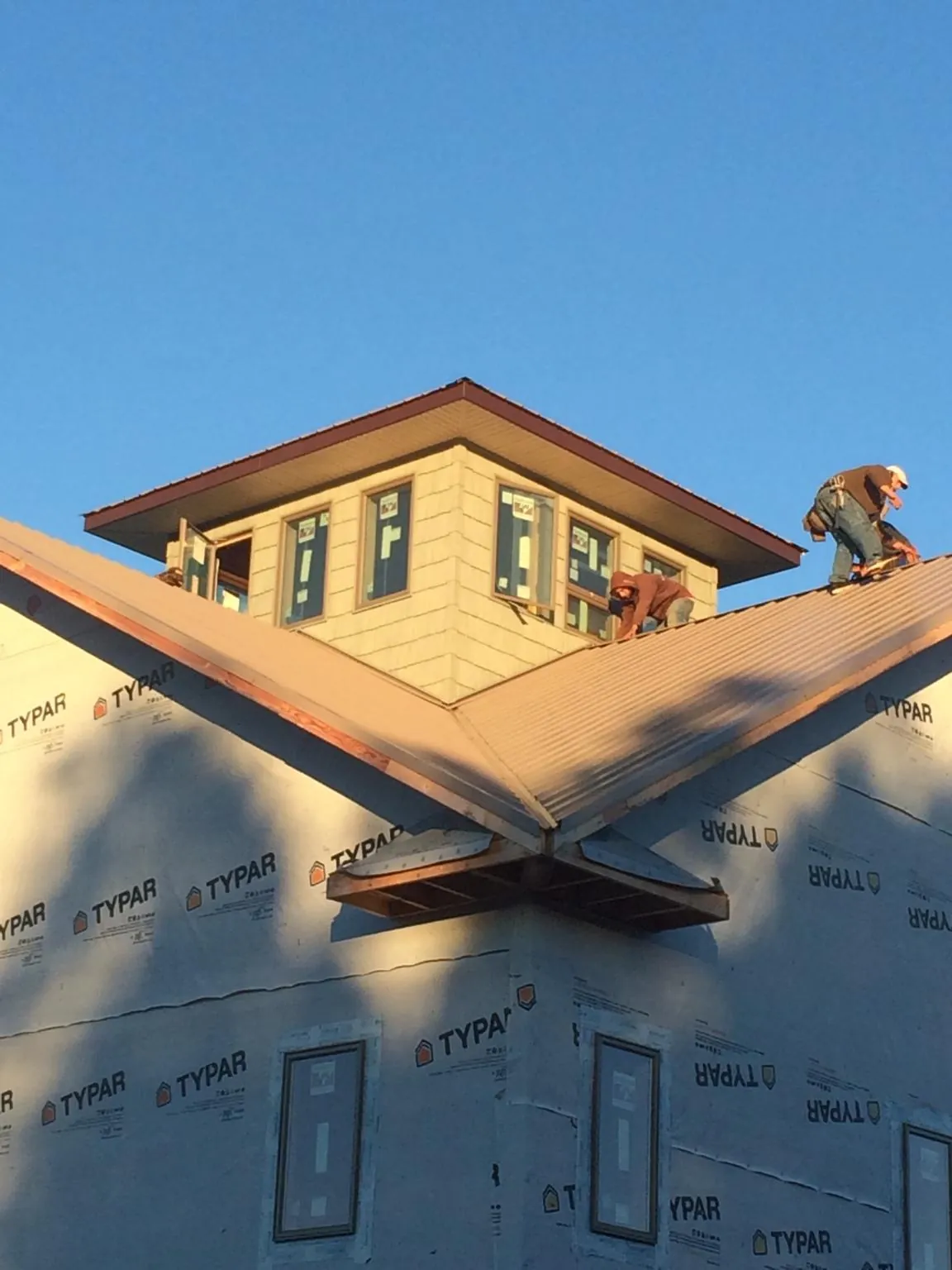 Roofers working around a rooftop cupola on a new metal roof at sunset — Roof Waterproofing in Delhi by Roofing Brothers